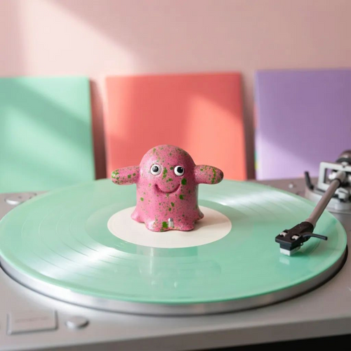 Pink clay ghost with green splatter and glitter finish, sitting on the spindle of a mint green record