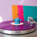Series 002 Vinyl Ghost on a purple record with colourful record sleeves behind