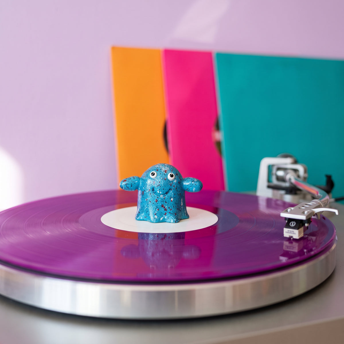 Series 002 Vinyl Ghost on a purple record with colourful record sleeves behind